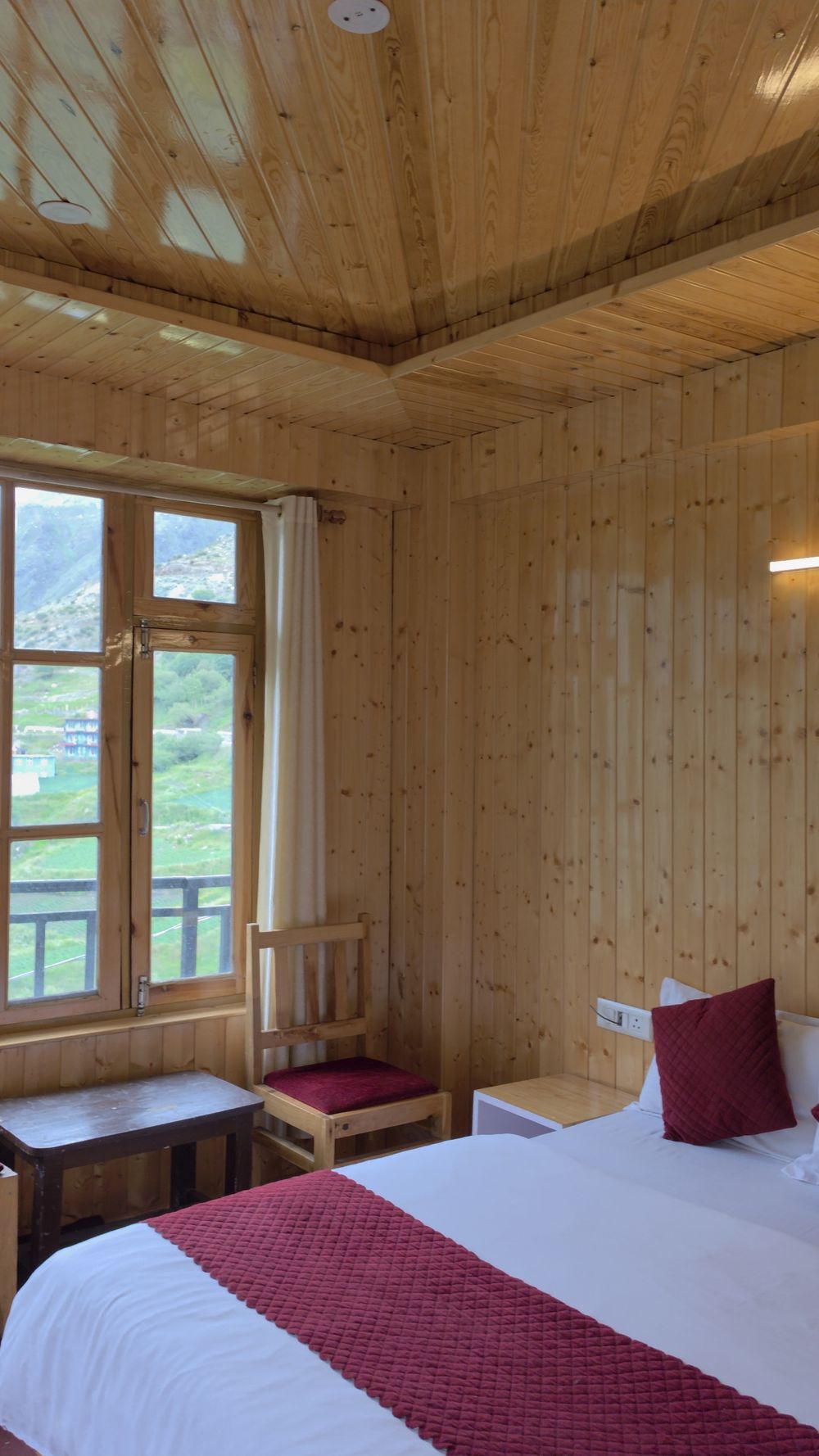 Pine-panelled deluxe valley-view room with a large mountain-facing window and warm bedding